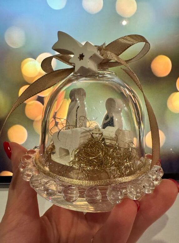 Presepe artigianale in miniatura all’interno di una cloche di vetro, con dettagli raffinati che evocano l’atmosfera del Natale.